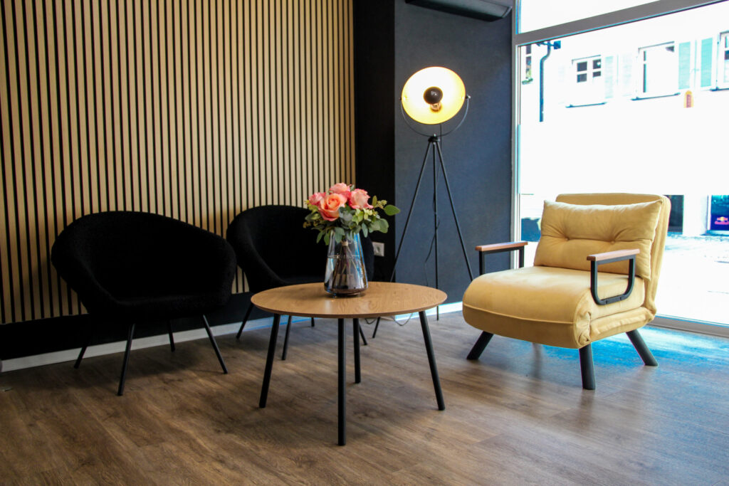 Moderner Wartebereich im Hautstudio Amy in Ravensburg mit stilvollen Sesseln, Holzwand, Stehlampe und frischen Blumen